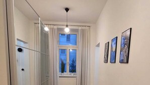 A hallway with a wooden floor, a large mirror, a window with curtains, and framed pictures on the wall. - Schönbrunn Apartment - Spacious and Tastefully Decorated, Close to the City Center (Wien)