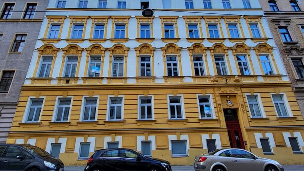 A multi-story building with a yellow facade, multiple windows, and a red door. - Schönbrunn Apartment - Spacious and Tastefully Decorated, Close to the City Center (Wien)