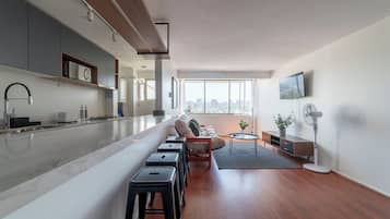 Uma cozinha moderna com uma ilha central, área de refeições com sofá e cadeiras, e uma grande janela com vista para a cidade.