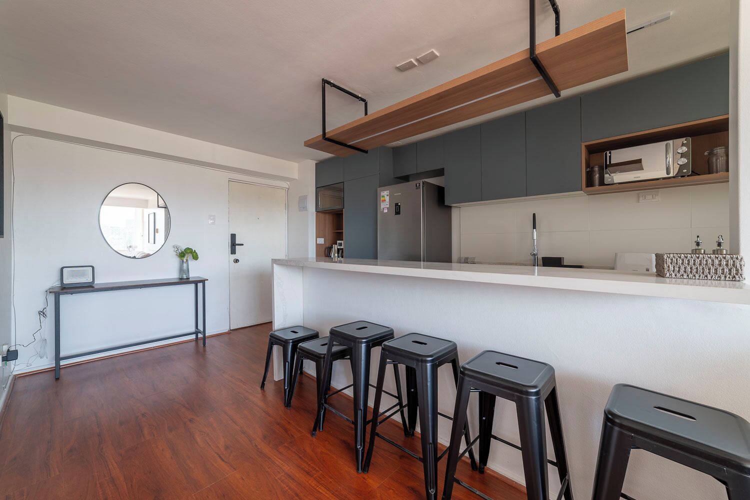 Cozinha moderna com ilha central, banquetas e luminária pendente.
