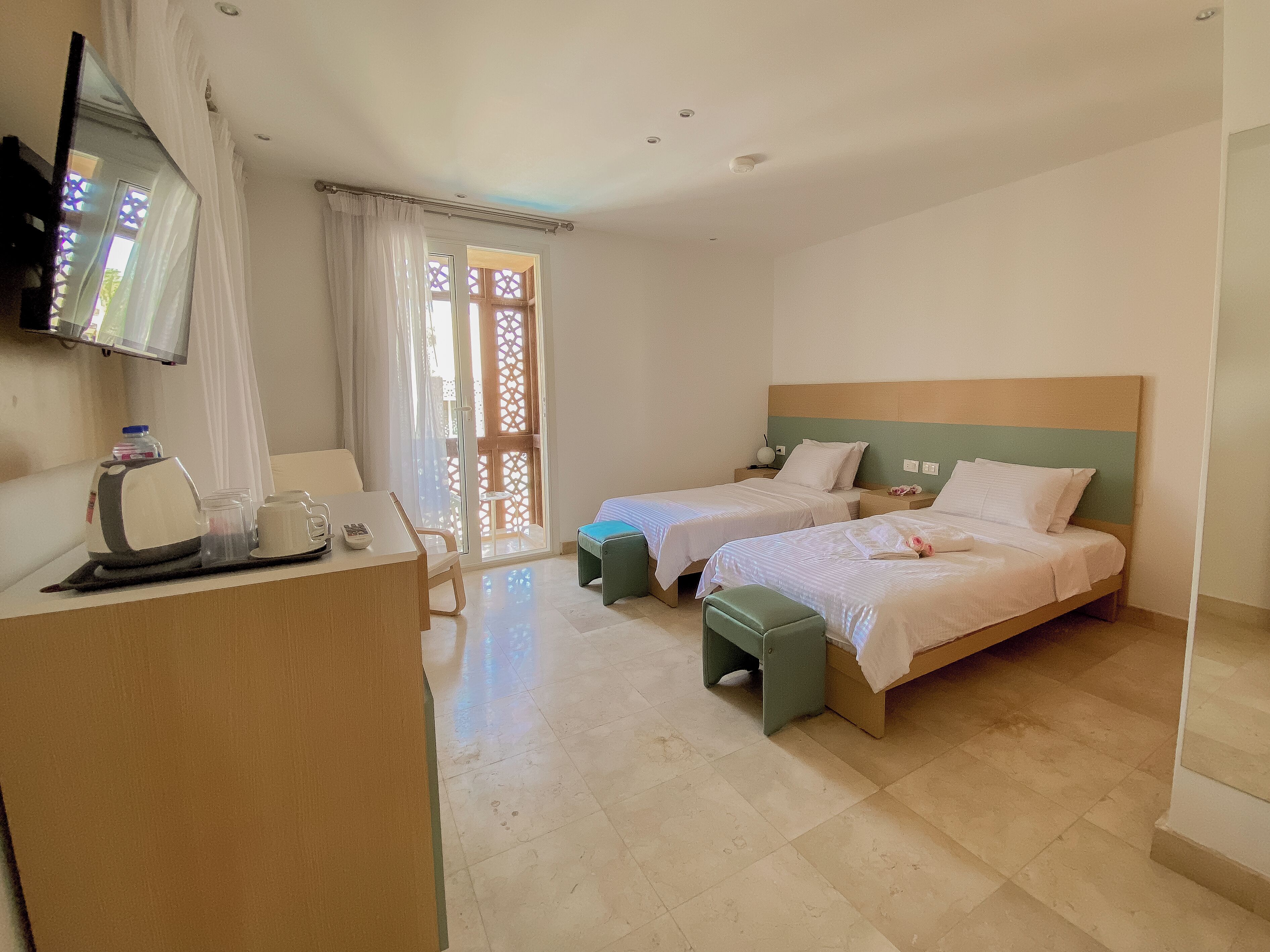 Habitación de hotel con dos camas, un escritorio y teléfono, un televisor montado en la pared y un ventanal corredero que da a un espacio exterior.