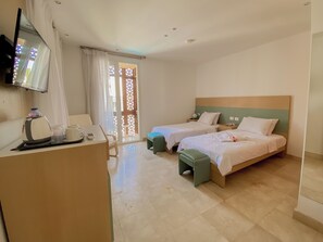 Ein Hotelzimmer mit zwei Betten, einem Schreibtisch mit Telefon, einem an der Wand befestigten Fernseher und einer Glasschiebetür zu einem Außenbereich.