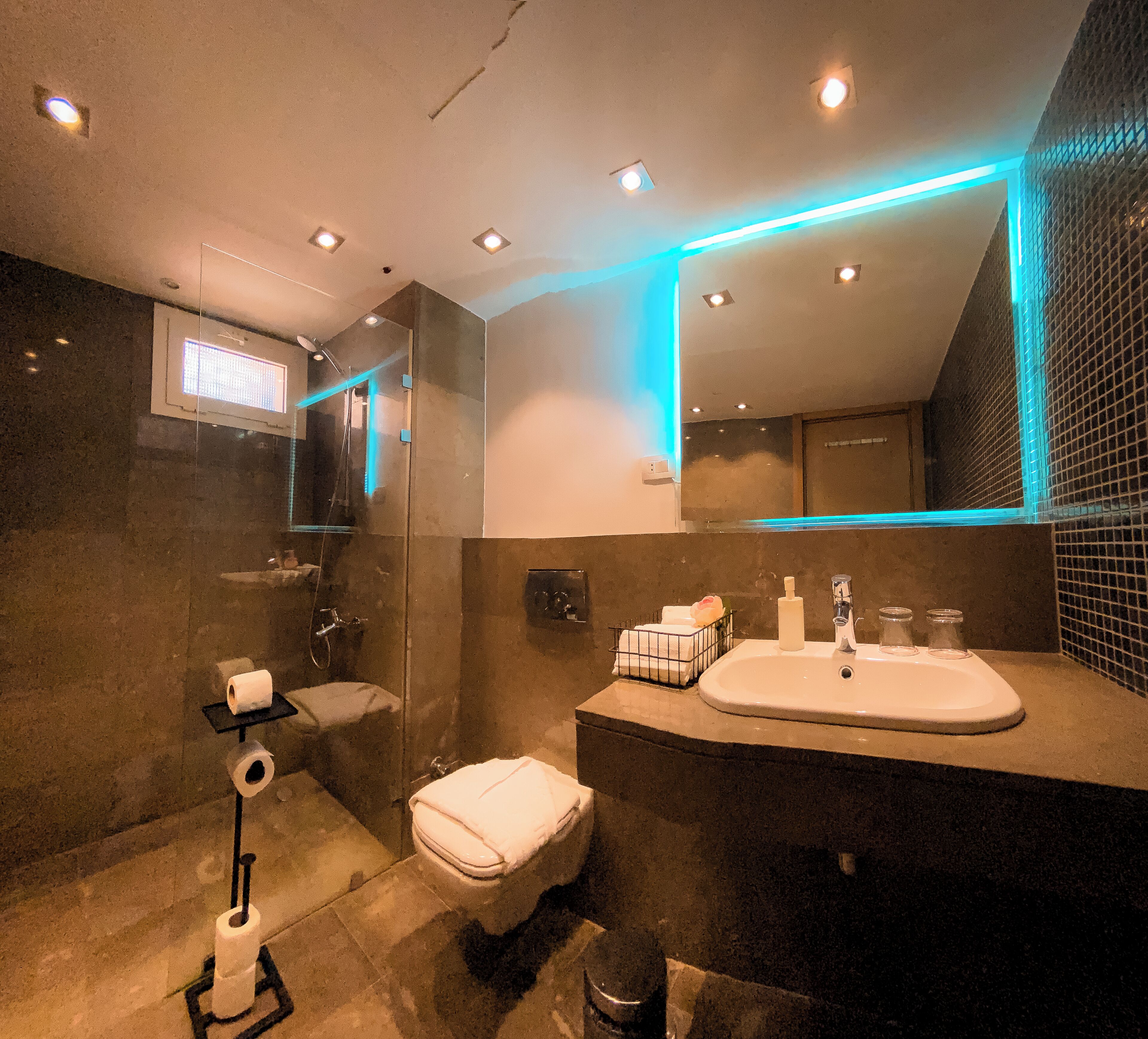 Une salle de bain moderne avec un grand miroir, des toilettes, un lavabo avec des articles de toilette et des spots encastrés au plafond.