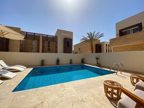 A rectangular swimming pool with clear blue water, surrounded by lounge chairs and potted plants.