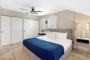 Een slaapkamer met een bed, nachtkastje, lamp, plafondventilator en raam met gordijnen.