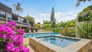 A swimming pool with a stone border, surrounded by lounge chairs and tropical plants. - Front row for Bali Hai and  BEST sunsets on Kauai  @ Pali Ke Kua (Princeville)