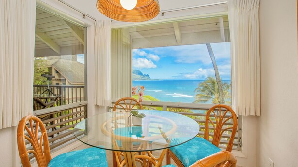 A round glass table with wicker chairs, a view of the ocean, and a balcony with a railing. - Front row for Bali Hai and  BEST sunsets on Kauai  @ Pali Ke Kua (Princeville)