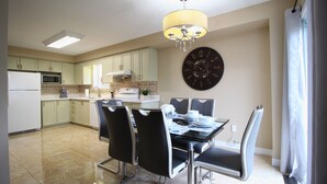 Una cocina moderna con armarios blancos, una mesa de comedor con sillas, una araña y un reloj de pared grande.
