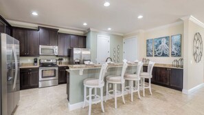 A modern kitchen with dark wood cabinets, stainless steel appliances, and a central island with bar stools. - Cosmic Clubhouse by Avantstay Sleeps 23 Arcade + Pool + Spa Mins to Disney (Kissimmee)