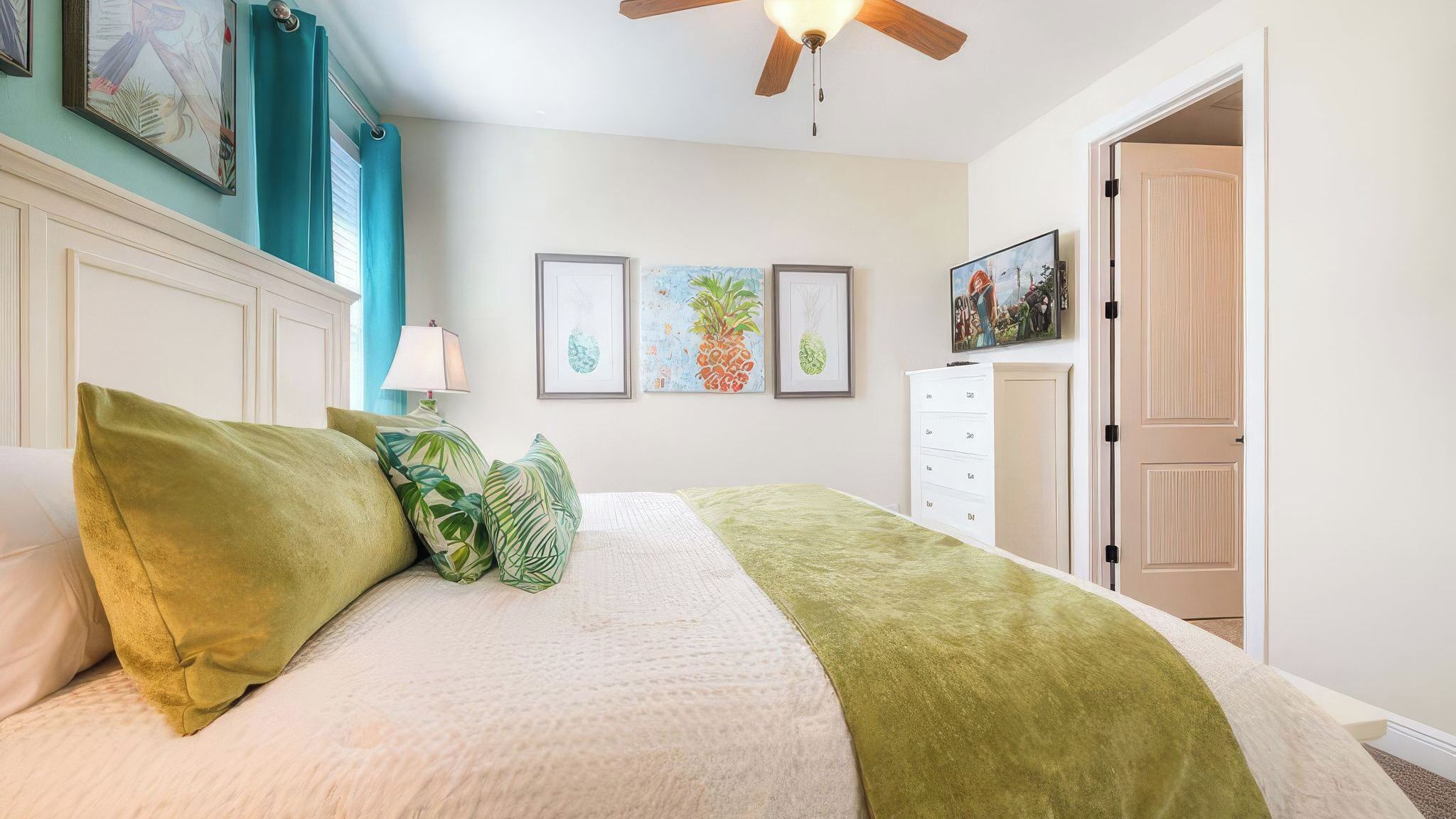 A bedroom with a bed, a ceiling fan, a nightstand, a lamp, a dresser, and framed artwork on the wall.