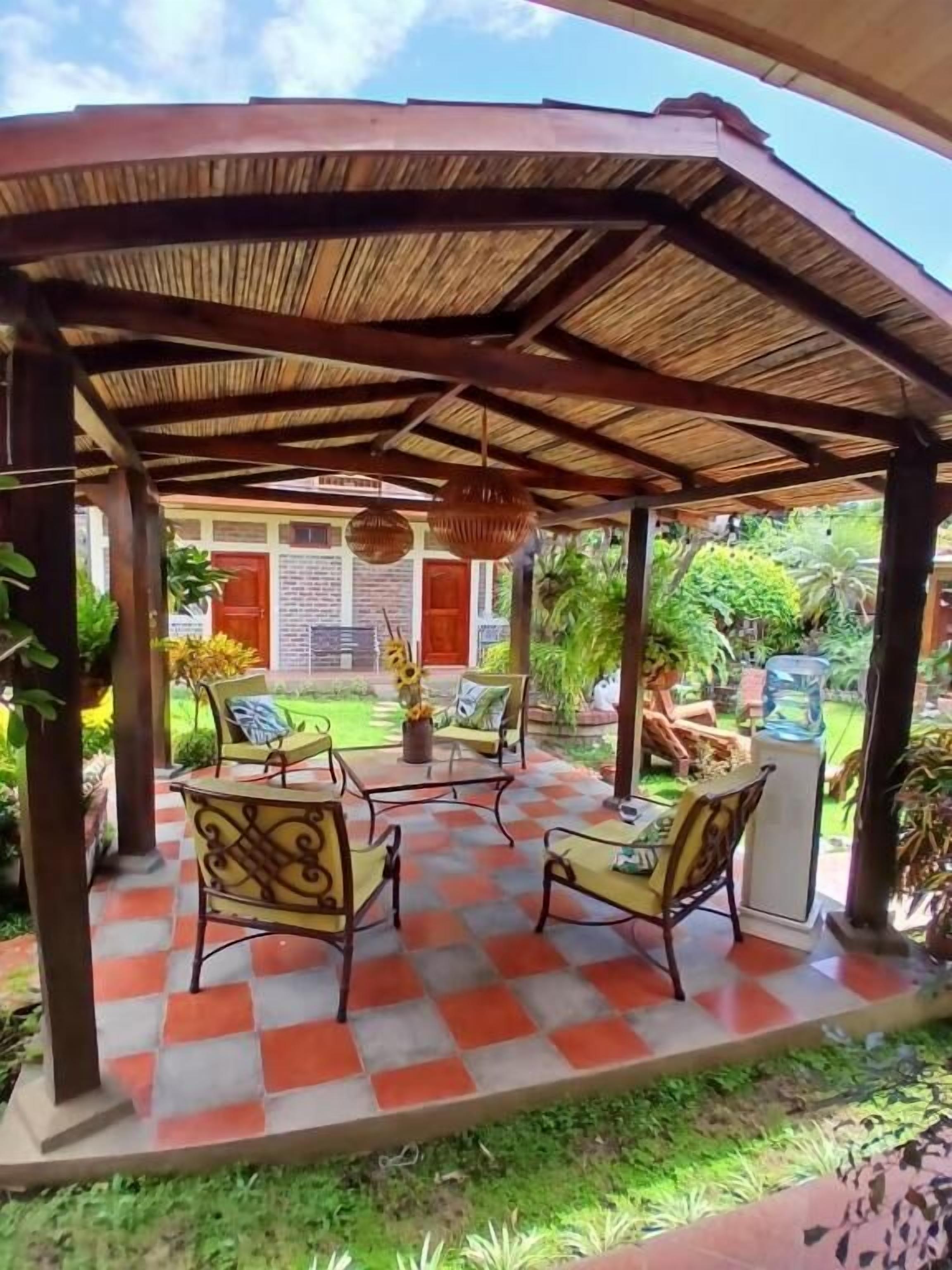 A covered patio with checkered flooring, outdoor furniture, and a view of a building with a red door.