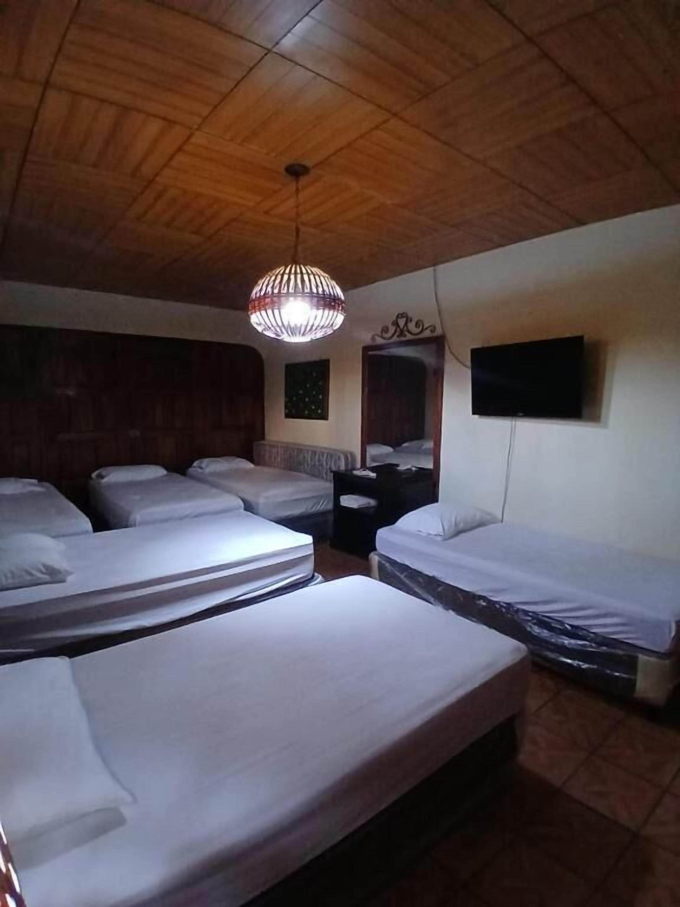 A room with wooden ceiling, multiple beds, a television, and a hanging light fixture.