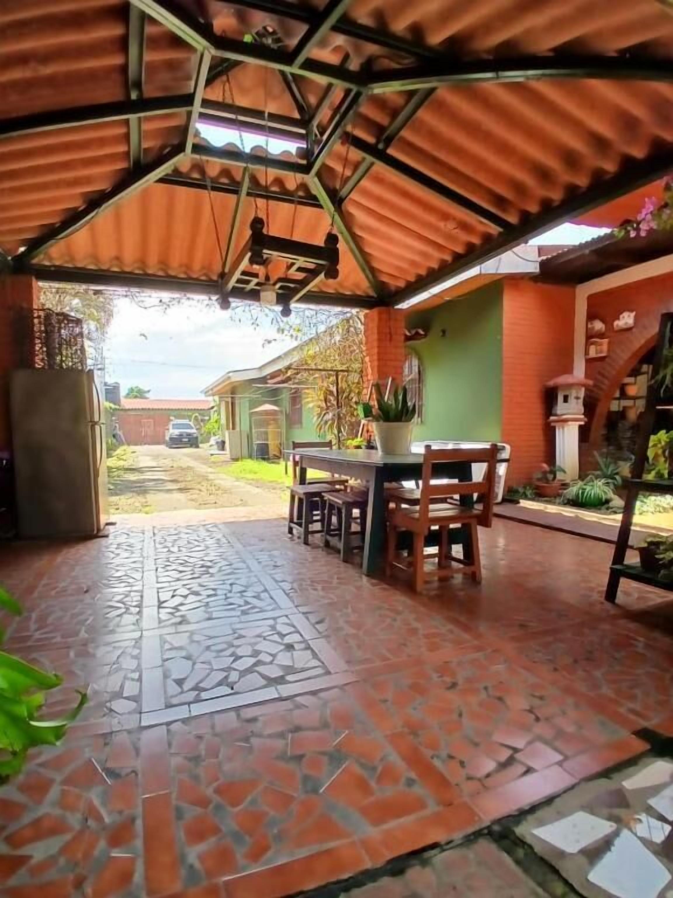 Un patio couvert avec un sol carrelé, une table avec des chaises et un luminaire suspendu.
