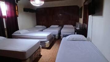 A room with four beds arranged in a row, wooden ceiling, and a hanging light fixture.