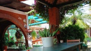 A covered outdoor dining area with a table and chairs, surrounded by potted plants and a brick archway. - Hostal Don Miguel (Rivas)