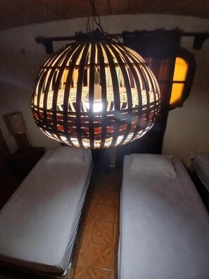 A room with two beds, a hanging light fixture, and a wall-mounted lamp.