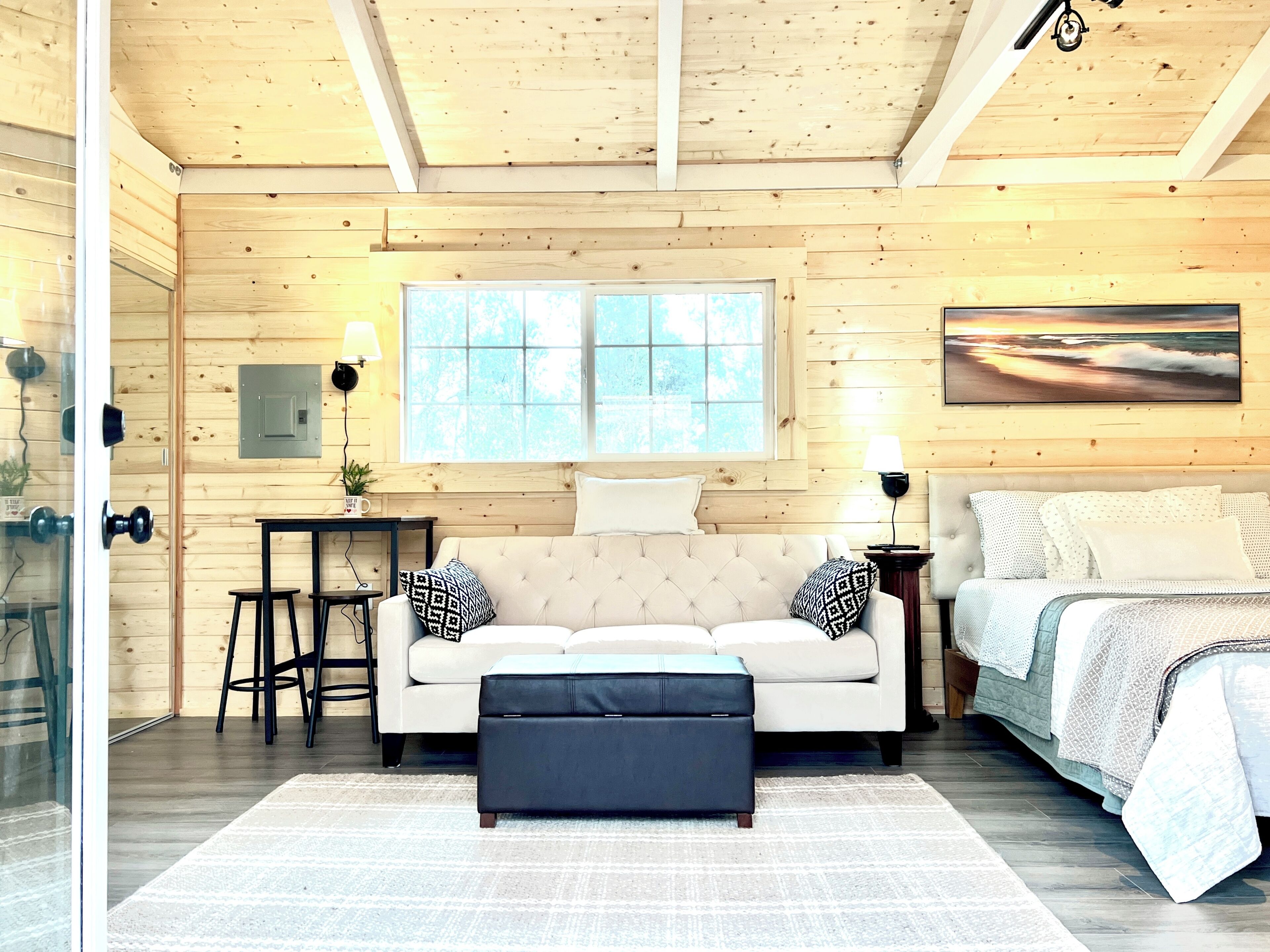 A cozy room with a sofa, ottoman, and a bed. There's a window with a view, a lamp, and a small table.