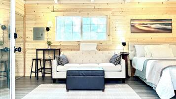 A cozy room with a sofa, ottoman, and a bed. There's a window with a view, a lamp, and a small table.
