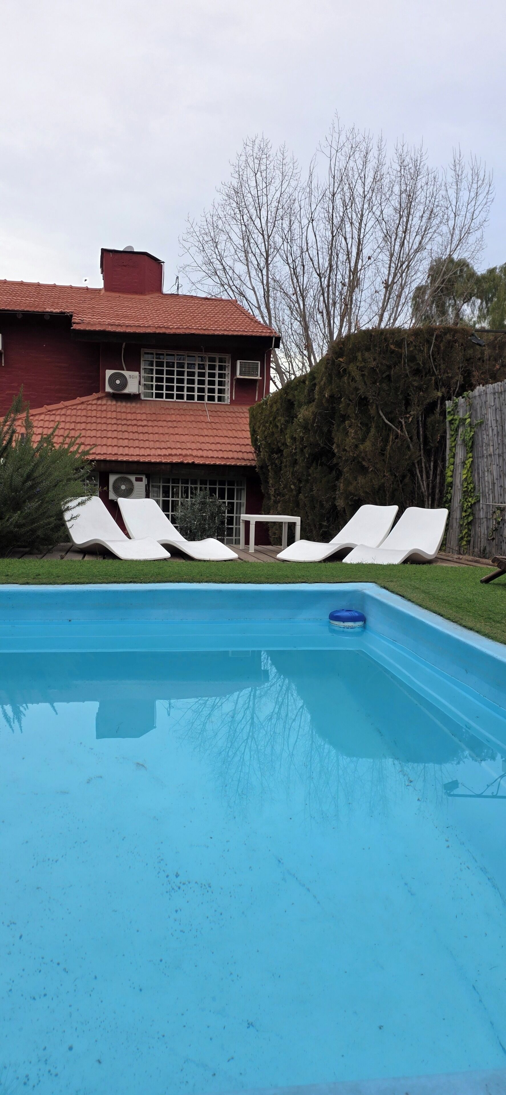A swimming pool with lounge chairs, a red building with air conditioning units, and a wooden fence.
