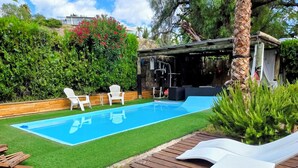 En baghave med swimmingpool, træterrasse, liggestole og et palmetræ.