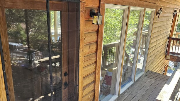 Eine Holzhütte mit großen Schiebeg lassfenstern, einer Holzterrasse und einem kleinen Veranda-Bereich.
