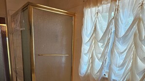 Ein Badezimmer mit einer großen Badewanne, einer Duschkabine und einem Fenster mit leichtem Vorhang.