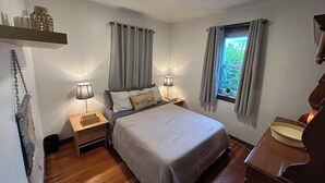 Una camera da letto con un letto, due lampade da comodino, una finestra con tende, un tavolino e una cassettiera in legno.