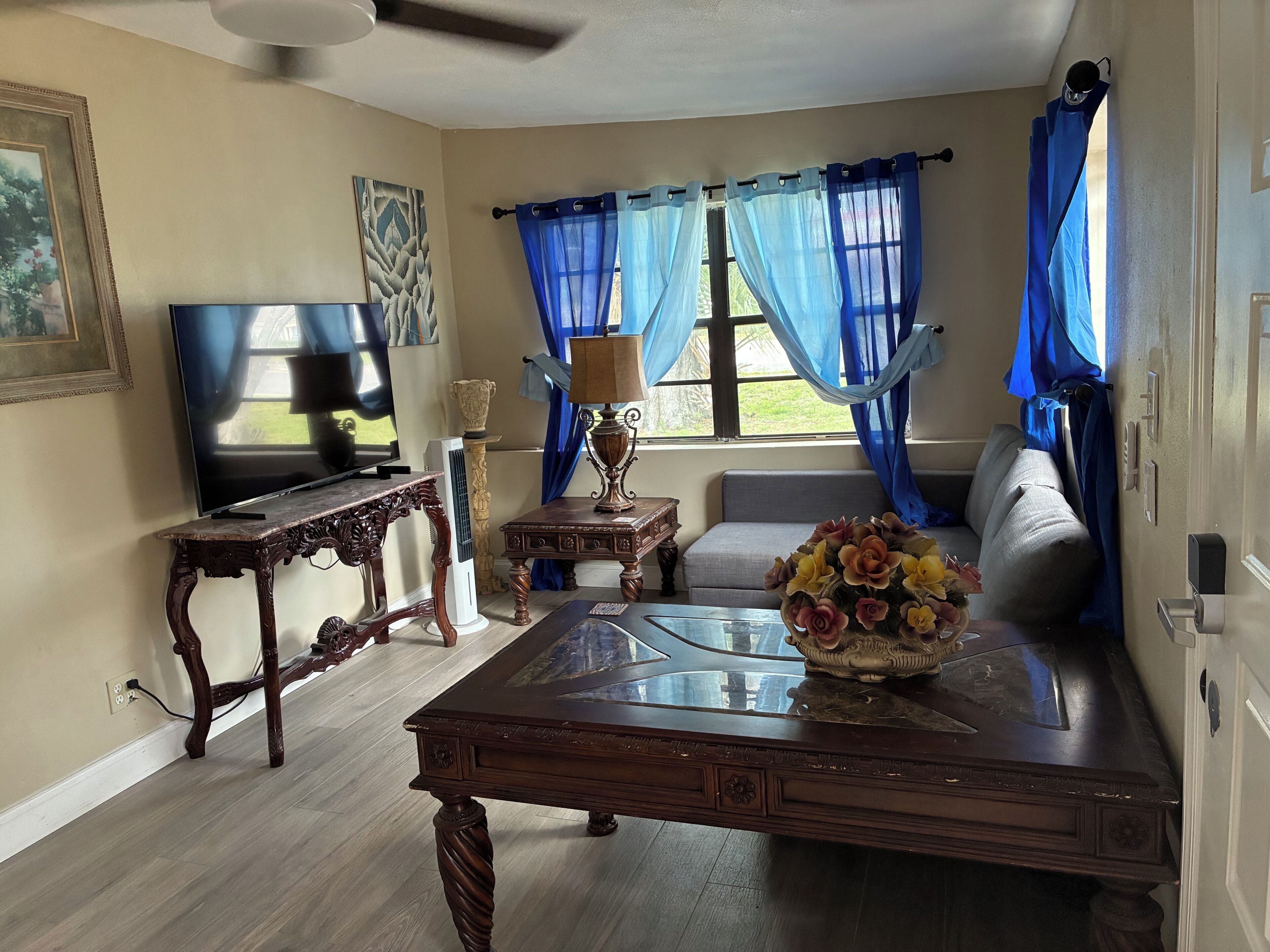 A living room with a TV, a decorative table, a sofa, and a window with blue curtains.