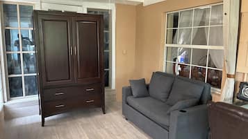 Una habitación con un armario de madera oscura, un sofá gris y un amplio ventanal con cortinas.