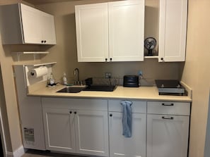 Una cocina con gabinetes blancos, un lavamanos de acero inoxidable, un tostador y un ventilador.