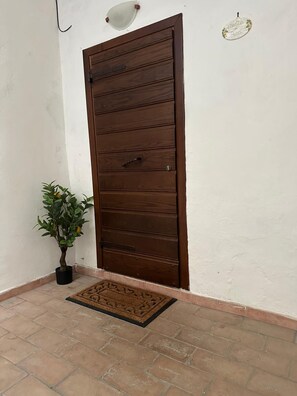 Eine braune Holztür mit Griff, einem Blumentopf und einer Fußmatte.