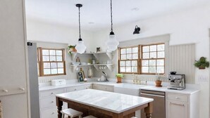 Uma cozinha com ilha de mármore, banquetas de madeira, luminárias pendentes e uma máquina de café.