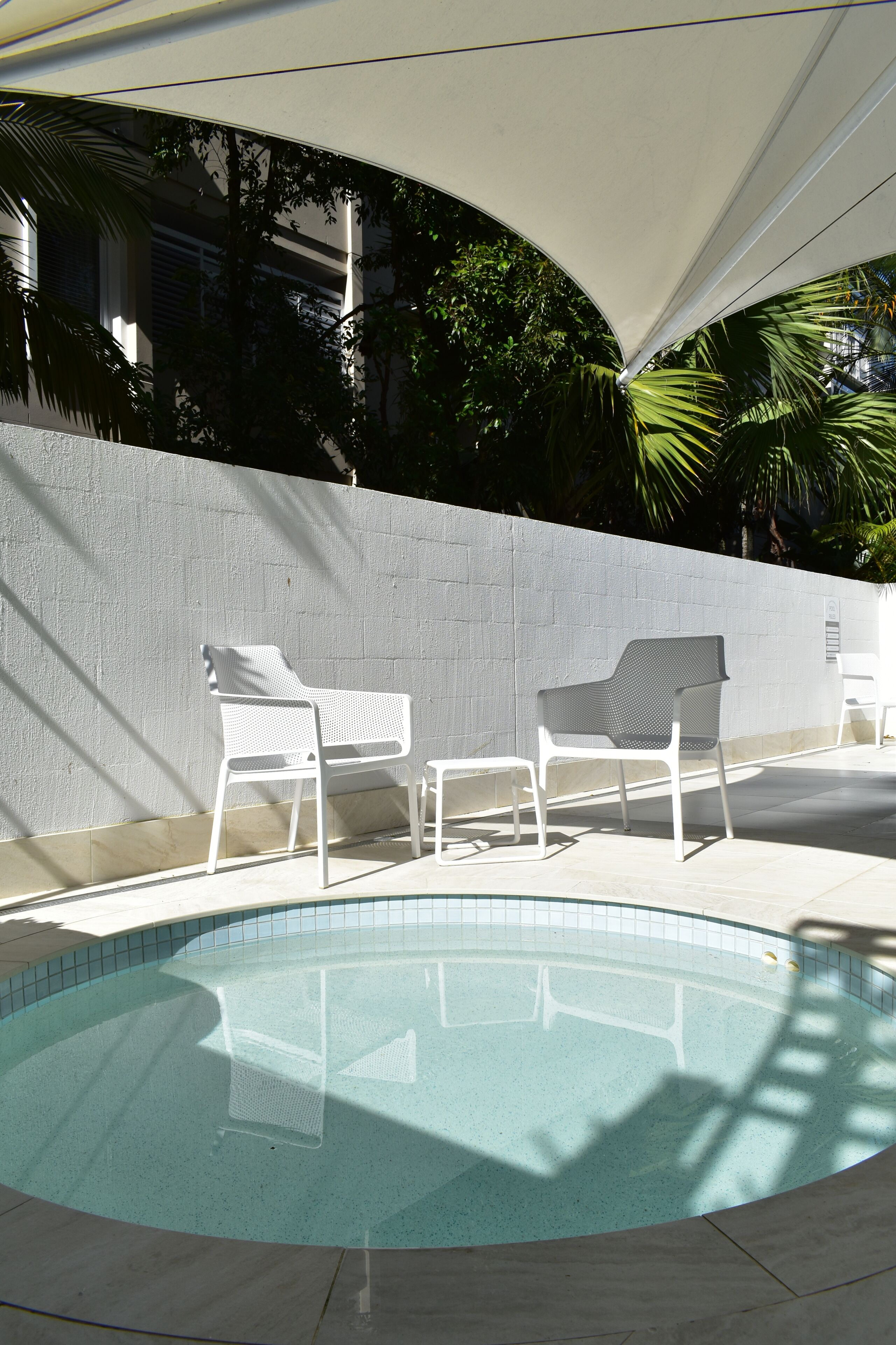 Une piscine avec deux chaises longues blanches et un mur blanc en arrière-plan.
