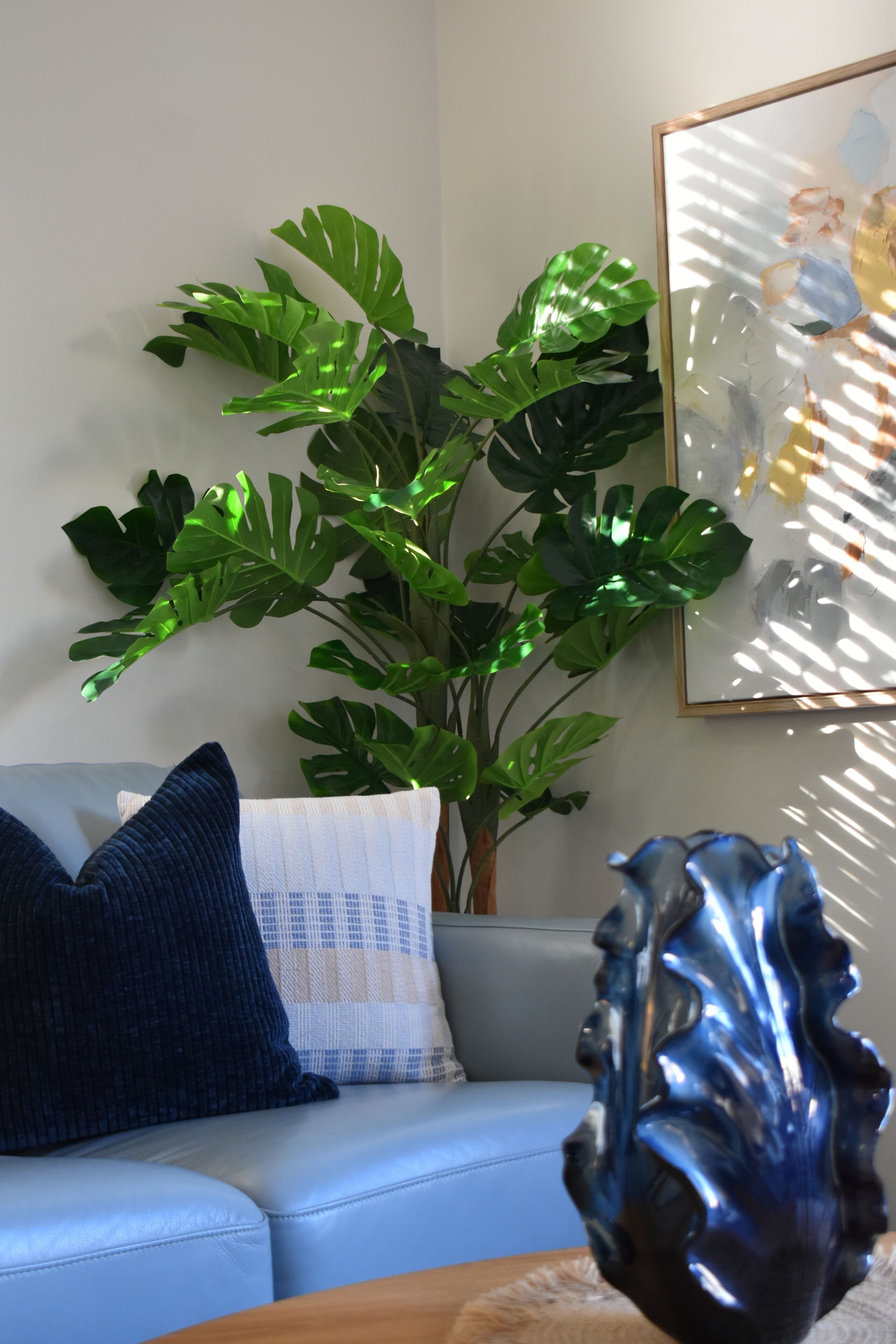 A room with a blue sofa, a large green plant, and a decorative sculpture.