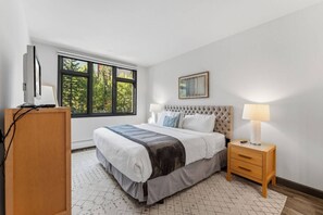 A bedroom with a bed, bedside table, lamp, and a window with a view of trees. - Ski-in ski-out Beaver Creek W/pool and hot tub (Beaver Creek)