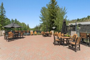 An outdoor patio with wooden tables and chairs, surrounded by trees and a brick floor. - Ski-in ski-out Beaver Creek W/pool and hot tub (Beaver Creek)