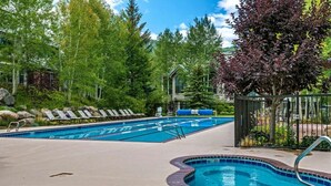 Una piscina con sillones de descanso, un jacuzzi y un jardín circundante.