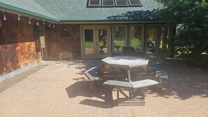 Een terras met een houten tafel en banken, een bakstenen muur en een overdekt gedeelte met glazen deuren.