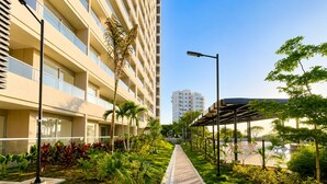Um caminho ladeado por vegetação, um edifício moderno com varandas e um céu claro.