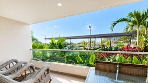 Varanda com mobiliário de vime, uma mesa de vidro e vista para um horizonte urbano com áreas verdes.