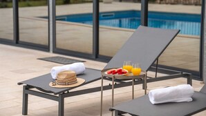 Zwei Liegestühle mit Handtüchern und eine Fruchtplatte mit Saft, mit Blick auf einen Swimmingpool.