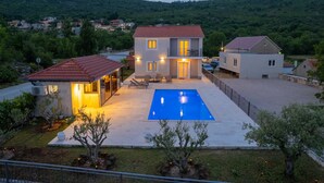Ein zweistöckiges Haus mit Swimmingpool, umgeben von Grünflächen und Hügeln.