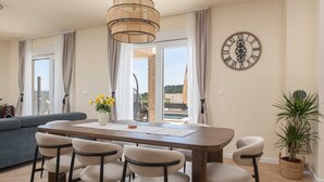 Een eetruimte met een houten tafel, zes stoelen, een vaas met gele bloemen en een wandklok.