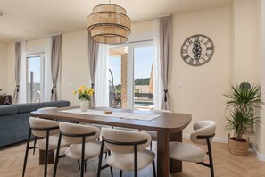 A dining area with a wooden table, six chairs, a vase with yellow flowers, and a wall clock. - Villa Ginger | Modern Villa with Private Pool (Tugare)