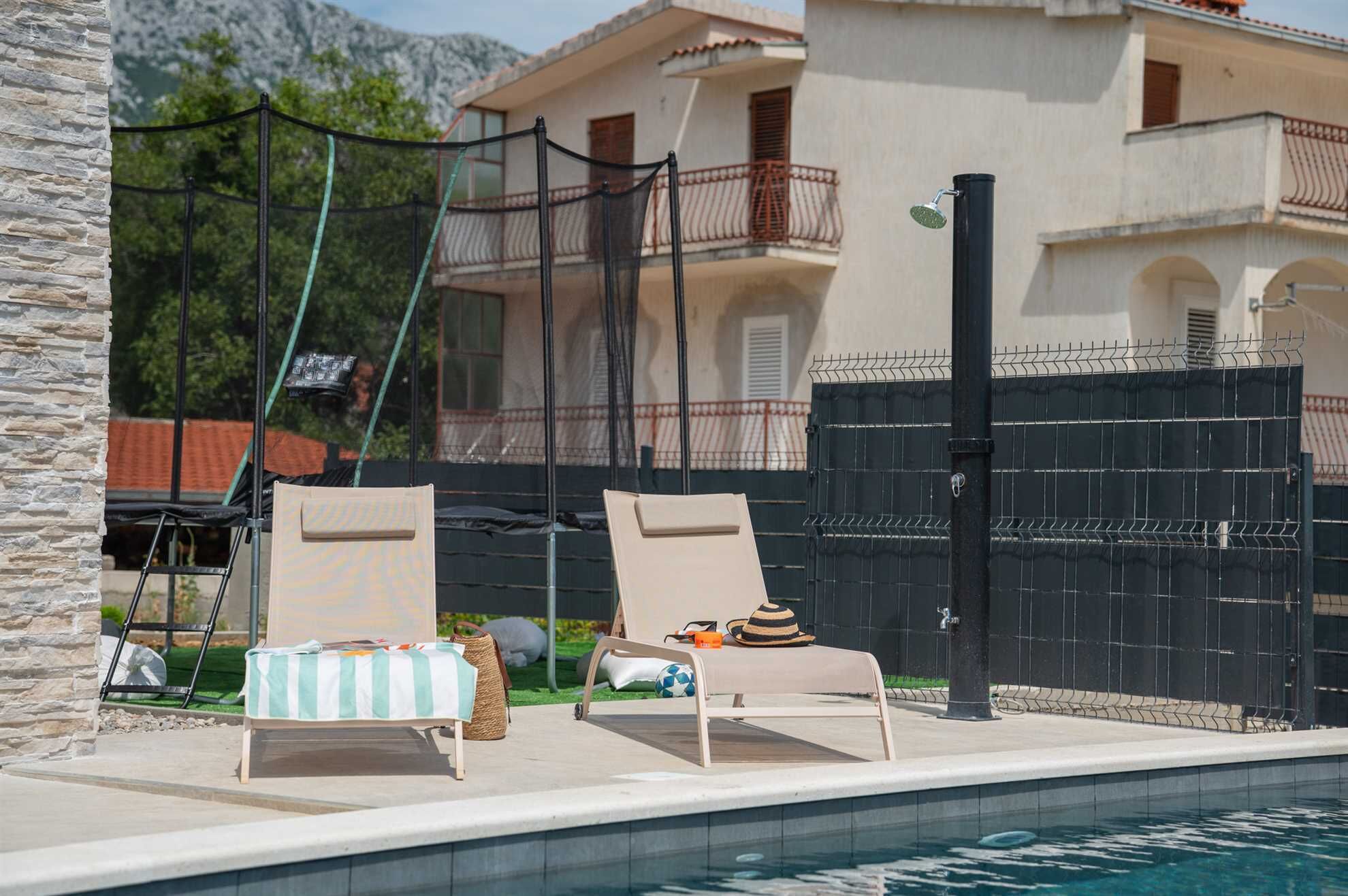 A poolside area with two lounge chairs, a small table with a striped tablecloth, and a hat on one of the chairs.