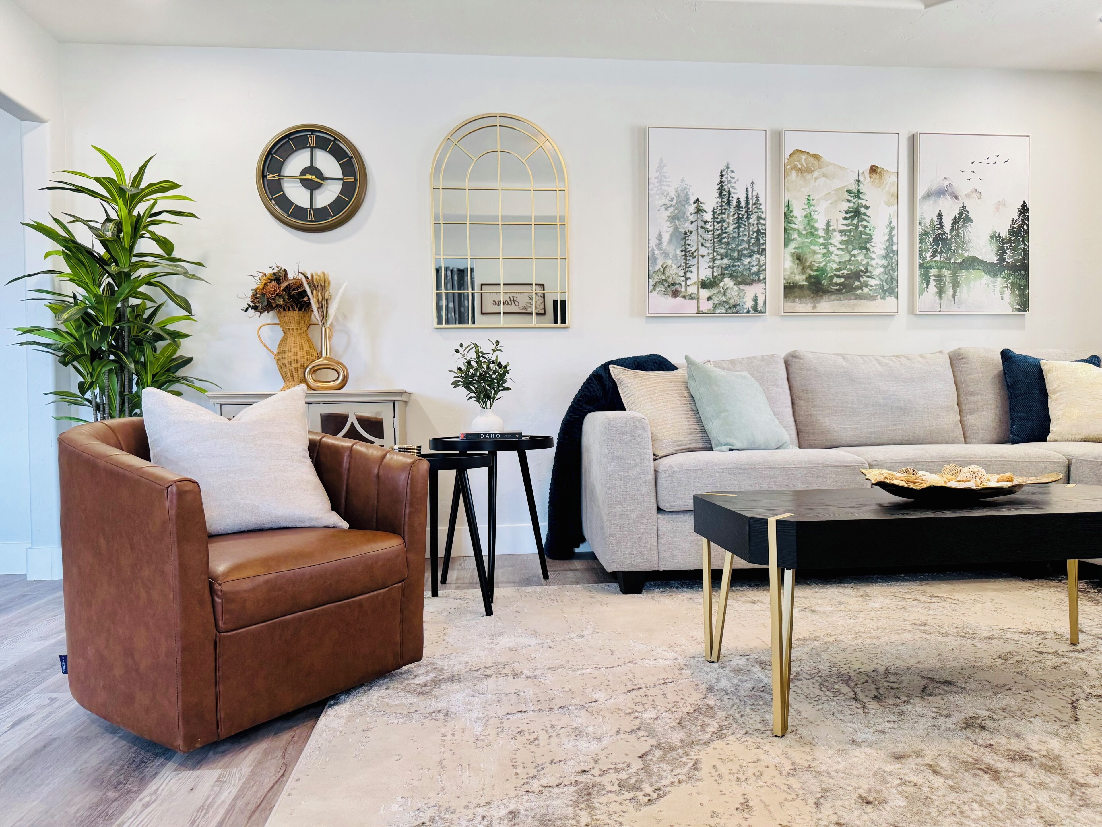 A living room with a brown leather armchair, a grey sofa, a black coffee table, a large mirror, and framed artwork on the wall.