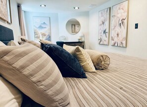 A bed with striped bedding, a round mirror, and floral artwork on the walls. - Entire Downtown Home - Yellowstone and Teton Base (Idaho Falls)