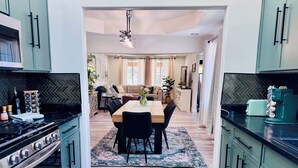 A modern kitchen with a dining area, featuring a stove, cabinets, and a coffee machine. - Entire Downtown Home - Yellowstone and Teton Base (Idaho Falls)