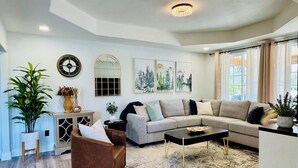 A living room with a sectional sofa, a coffee table, a brown armchair, a rug, a decorative mirror, wall art, and a clock. - Entire Downtown Home - Yellowstone and Teton Base (Idaho Falls)
