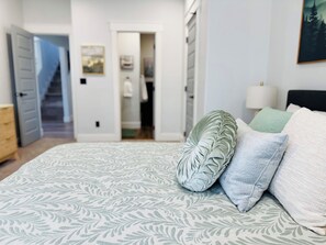 Una camera da letto con una coperta a motivi, cuscini, un comodino e una porta che dà su un'altra stanza.